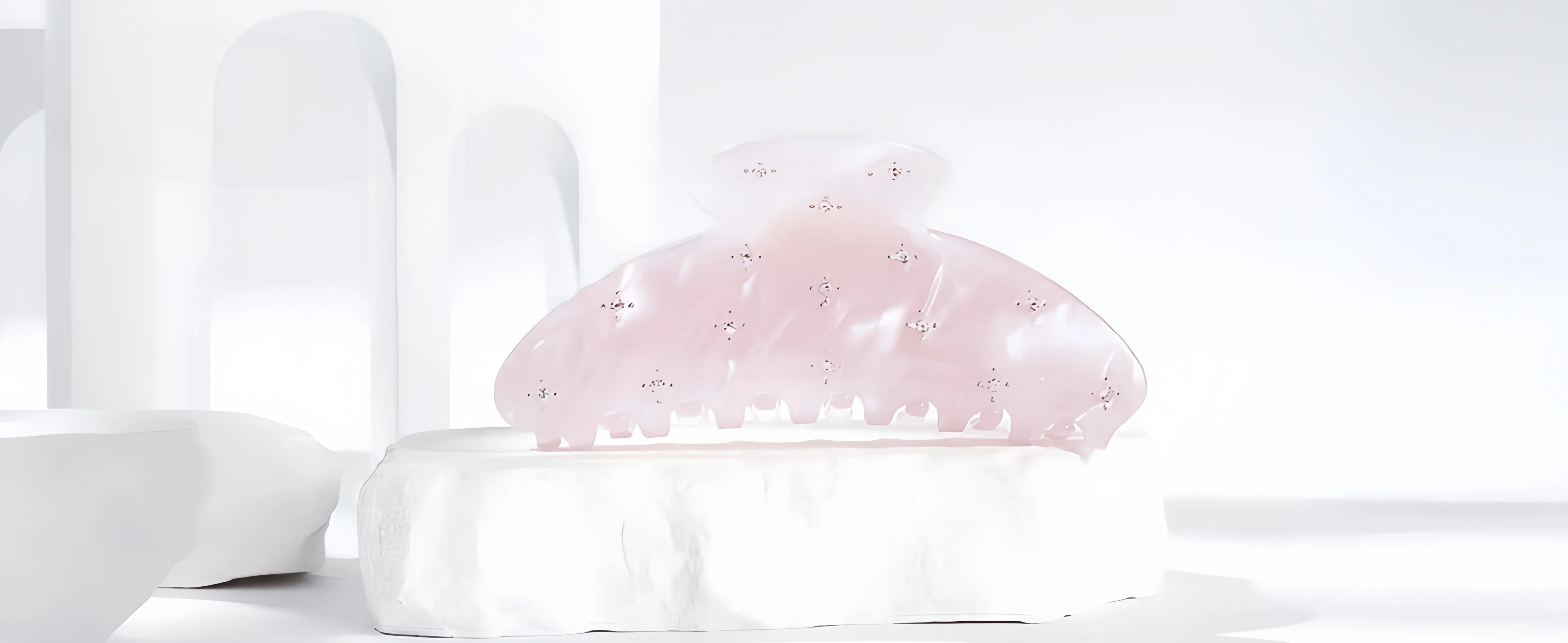 Glamup "The Emi" claw clip in a dreamy translucent pink acetate with scattered crystal embellishments, presented on a white textured display block against an ethereal white background.