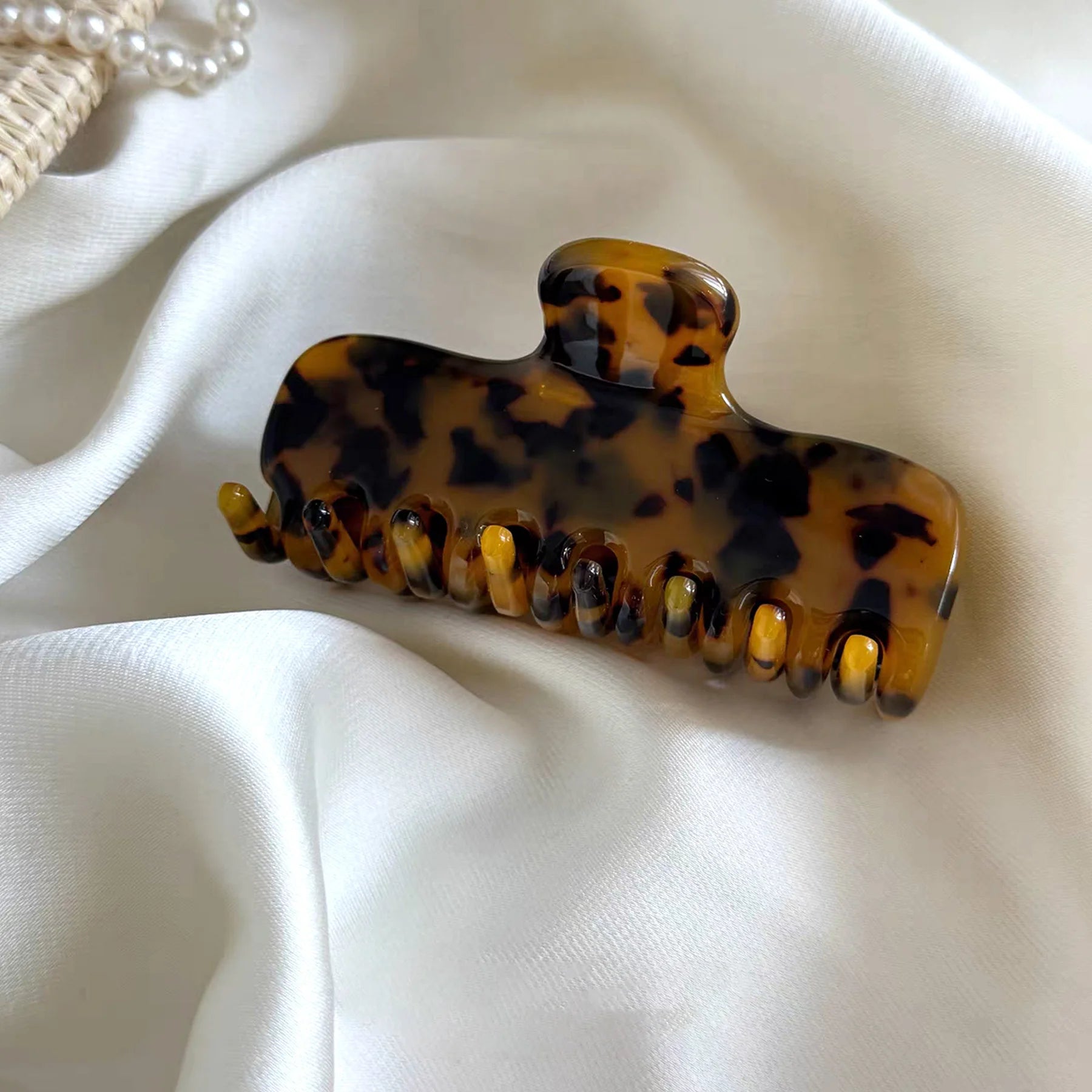 Glamup "The Jennie" tortoise acetate claw clip in a luxury styled setting with soft lighting, highlighting its rich pattern.