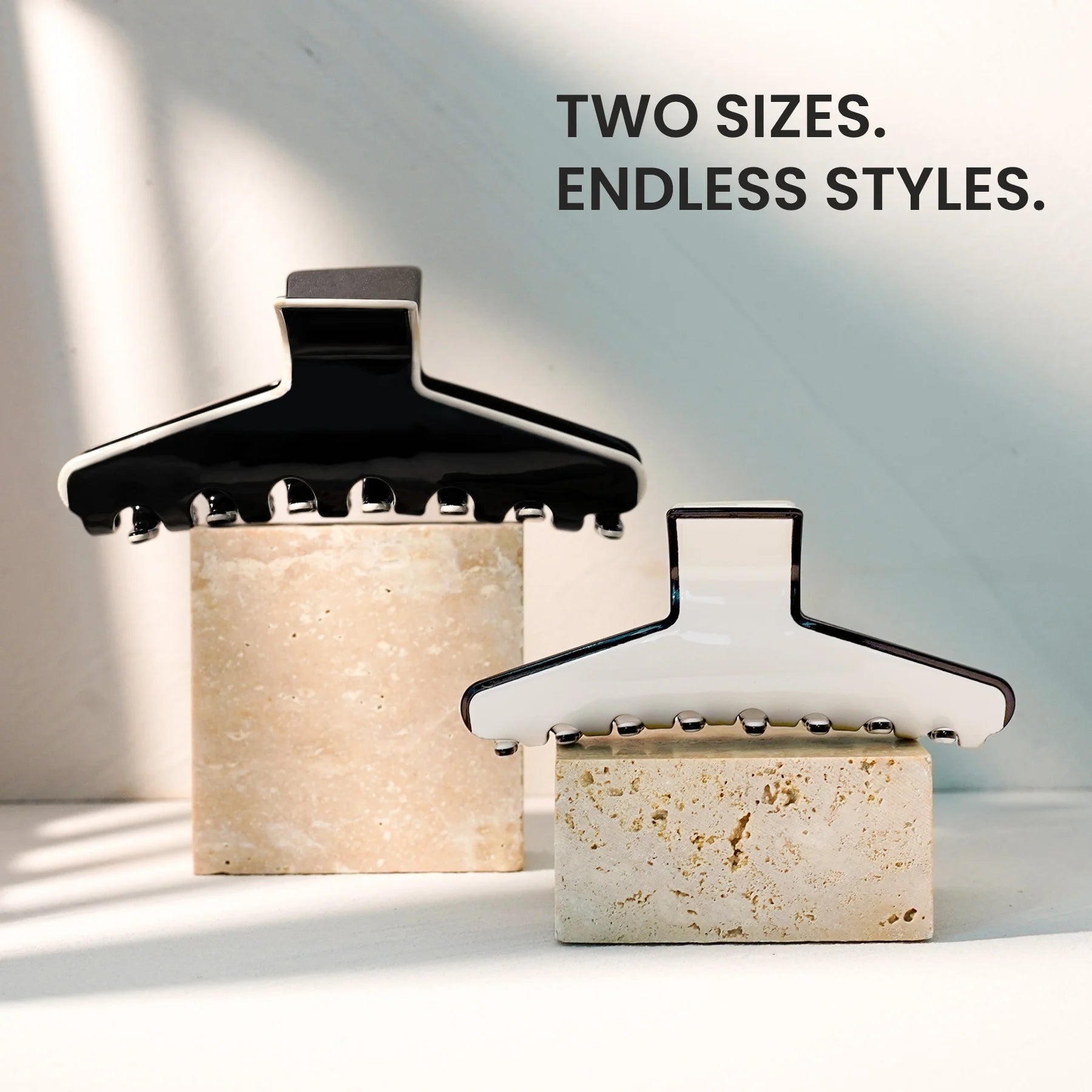Two sizes of The Kendall acetate claw clip displayed together on a stone surface, emphasizing versatile styling options.