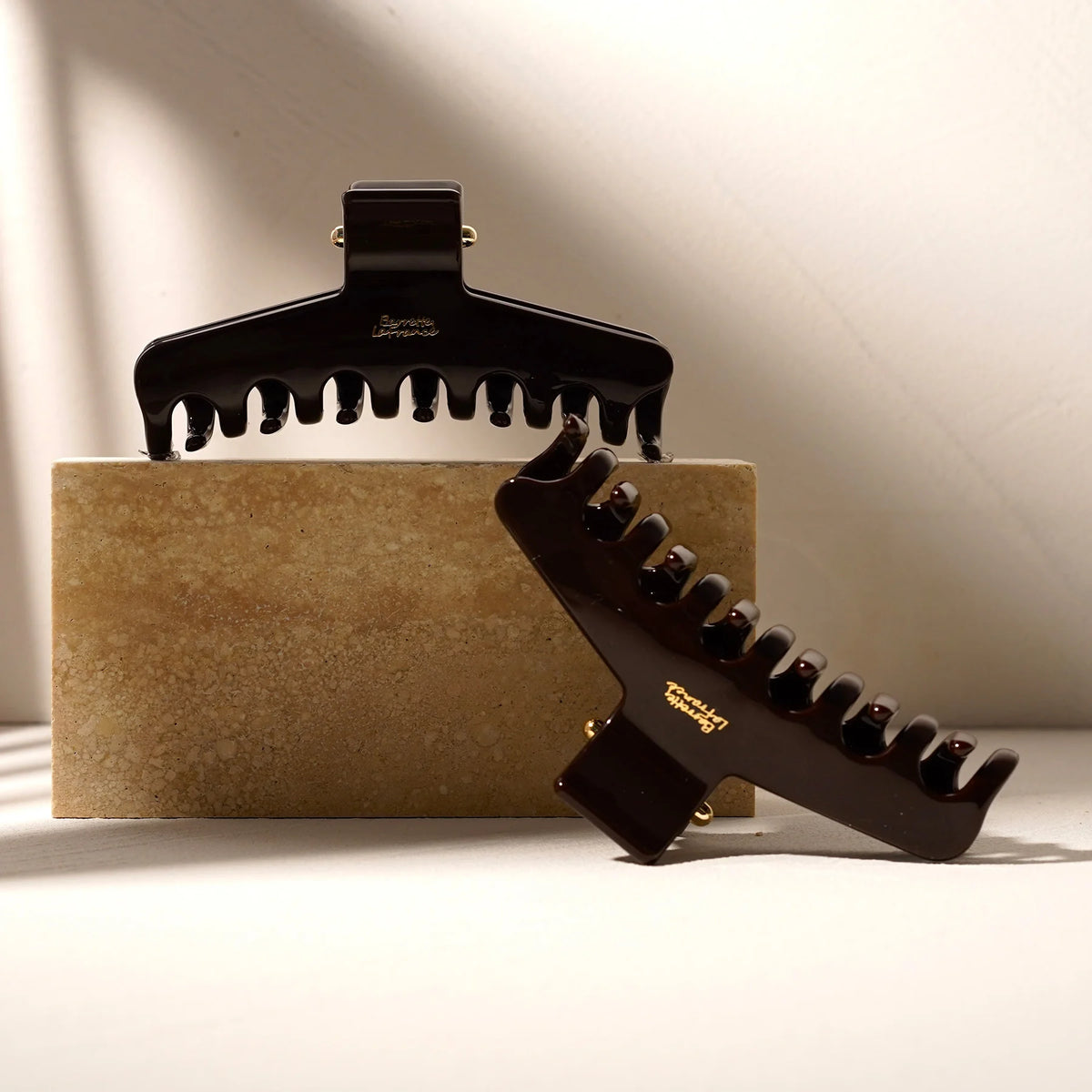 Two dark Glamup The Taylor XL jumbo size claw clips resting on a textured stone surface, showcasing their sleek finish and double-row teeth