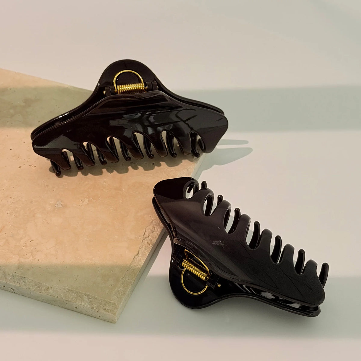 A pair of dark Glamup The Taylor claw clips angled on a stone slab, highlighting the XL jumbo size built with double-row teeth.